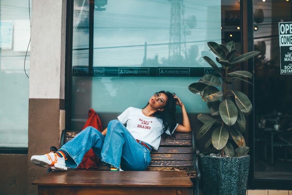 Fashionable woman in jeans and t-shirt relaxing on a bench outside a cafe.