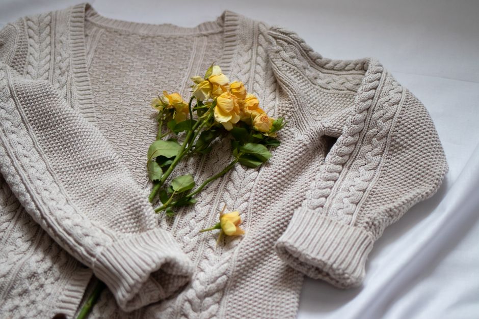 A beige cable-knit cardigan adorned with delicate yellow roses, evoking warmth and cozines