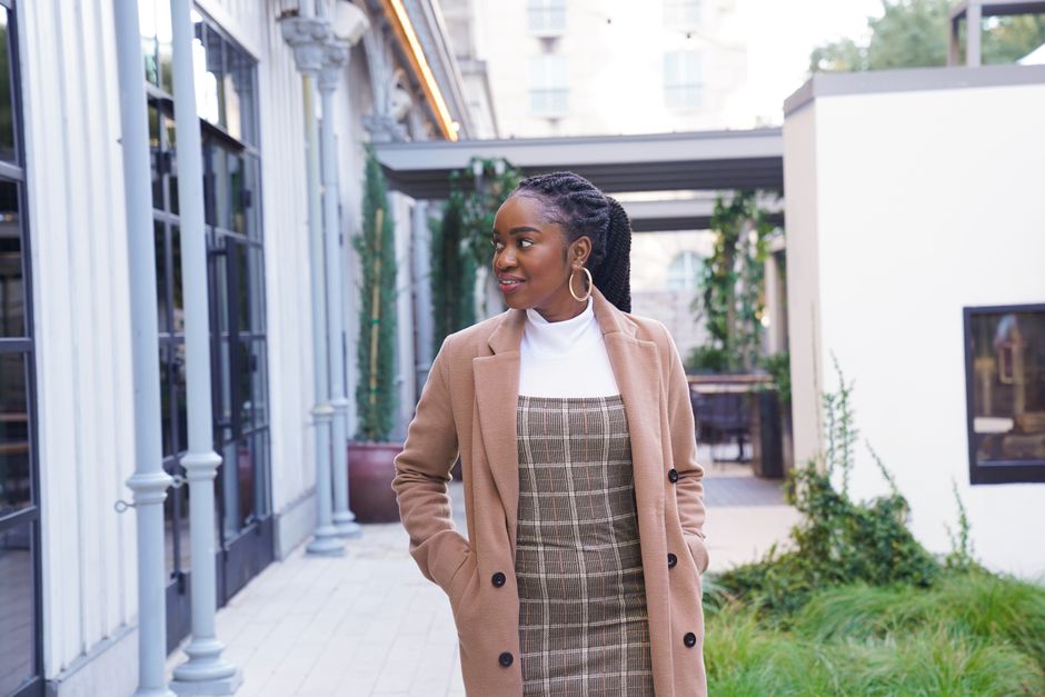 Young woman in a stylish brown jacket walking outdoors with a smile, showcasing fashion.