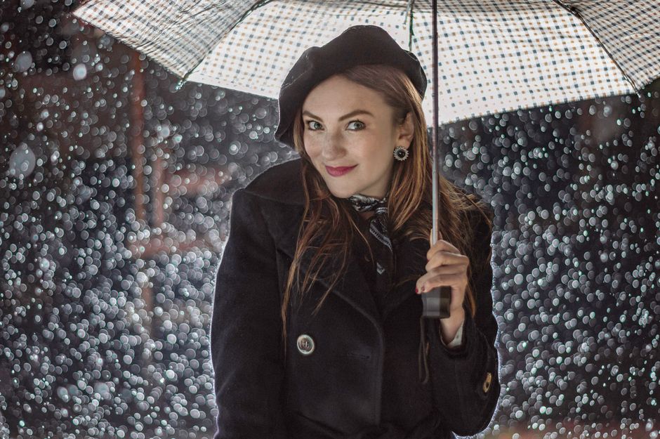 Portrait of a smiling woman in the rain holding a patterned umbrella.
