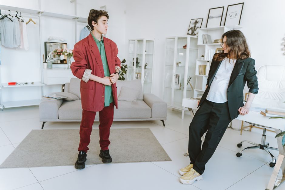 Stylish duo in red and black suits posing in a modern office interior, showcasing contemporary fashion.