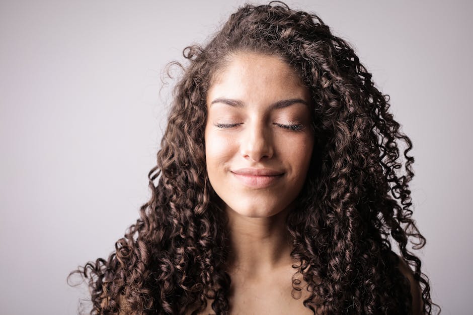A close-up portrait of a smiling woman with curly hair, eyes closed, exuding happiness.