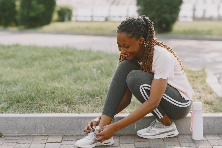 Smiling woman tying her sneakers while sitting outdoors on a sunny day, ready for a workout.