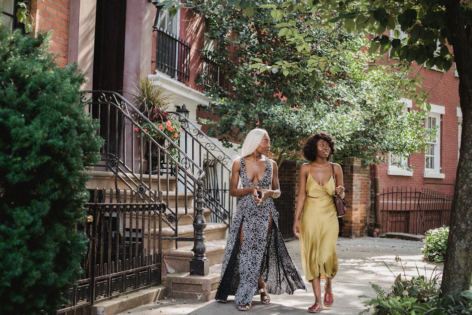 Two stylish black women walking and chatting outdoors on a sunny day in a charming urban neighborhood.