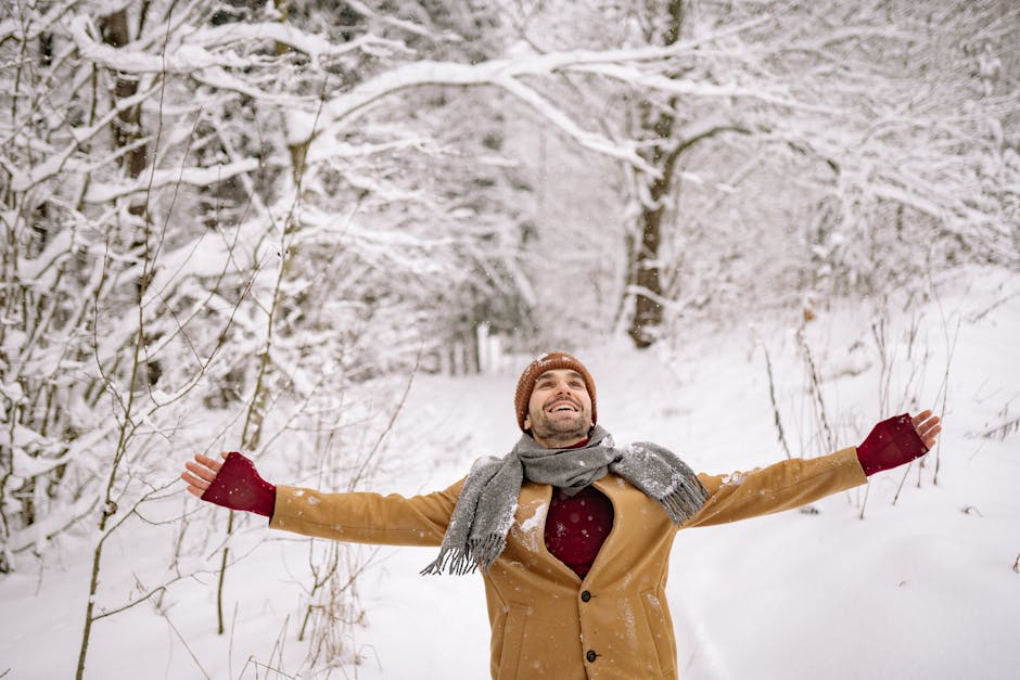Happy man in winter attire with arms outstretched in a snowy forest setting.
