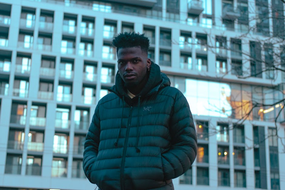 Stylish man in a jacket standing in front of a modern city building.