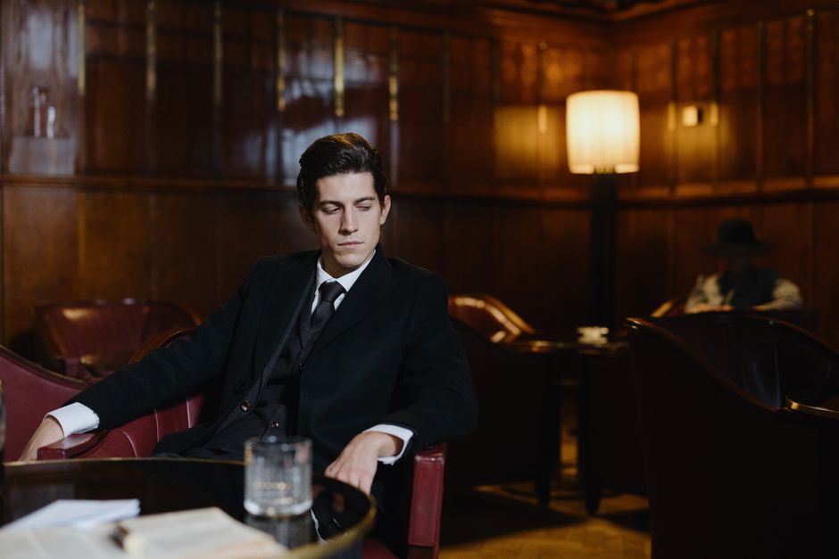 A well-dressed man sitting in a vintage lounge, exuding a sophisticated and contemplative mood.