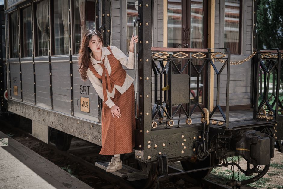 Stylish woman poses on a classic train, embracing vintage travel vibes.
