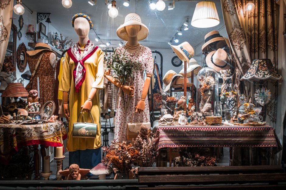 Charming vintage boutique window featuring dressed mannequins and ornate decor.