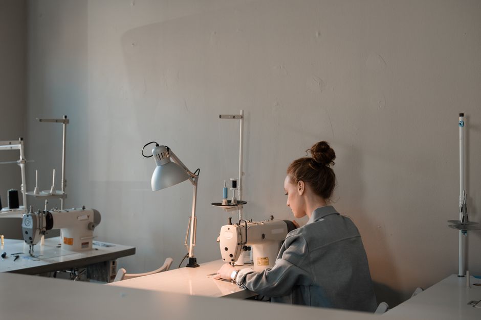 A female fashion designer working with a sewing machine in a well-lit studio.