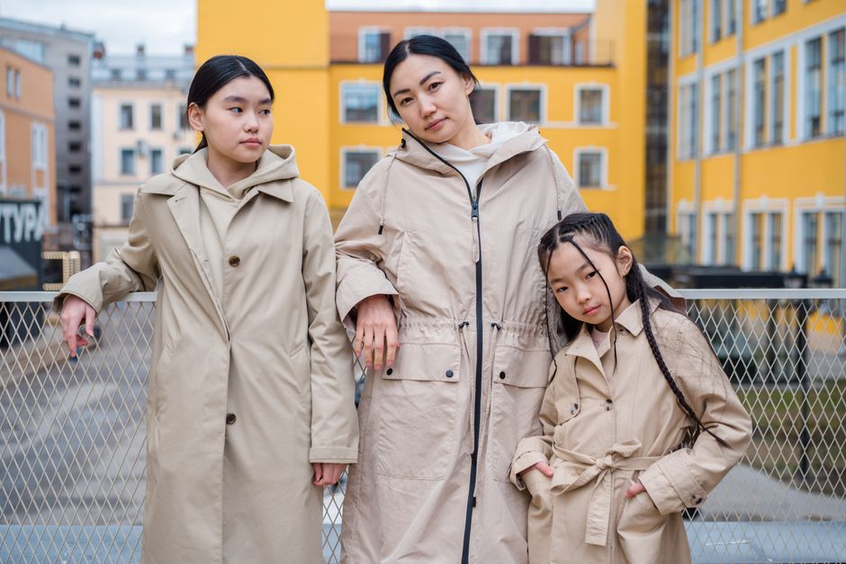 Family portrait of three in beige coats against vibrant urban backdrop.