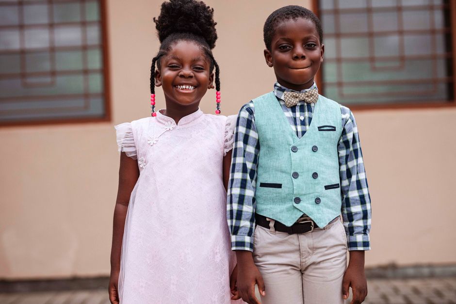 Adorable portrait of two smiling children in stylish outfits, outdoors in Accra, Ghana.
