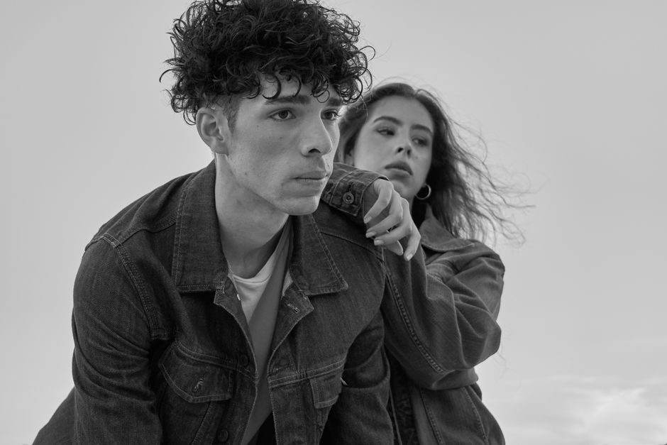 Black and white portrait of two young adults in denim jackets, capturing an intimate moment outdoors.