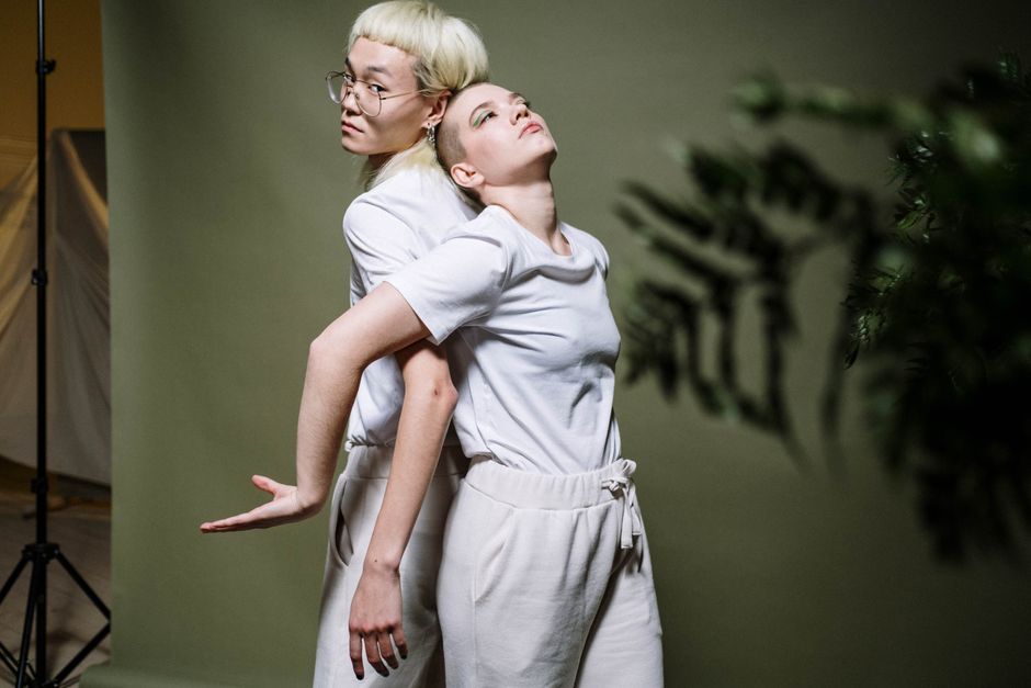 A creative studio portrait of two models in white clothing posing artistically against a green background.