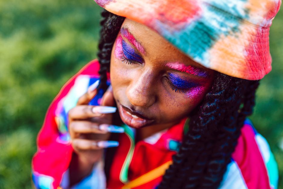Colorful portrait of a woman with vibrant makeup and a tie-dye hat outdoors.