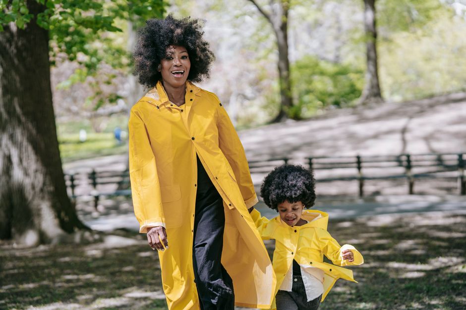 Joyful mother and child walking in yellow raincoats outdoors in the park.