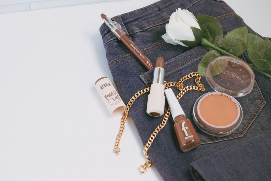 Stylish flat lay featuring makeup, denim, and a rose for a chic fashion statement.