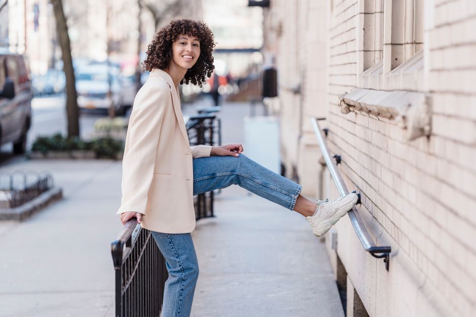 Side view of African American female leaning on metallic railing and looking at camera while putting foot on building wall