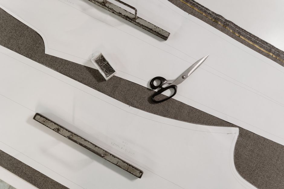 Detailed view of scissors, pattern paper, and fabric on a tailor's workbench.