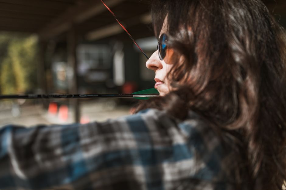 A woman practicing archery outdoors, aiming with concentration. Perfect shot capture.