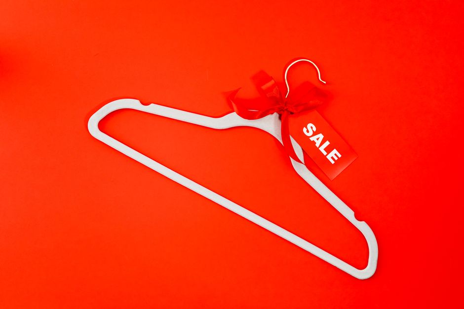 A white hanger with a red sale tag and ribbon on a vibrant red background, ideal for shopping promotions.