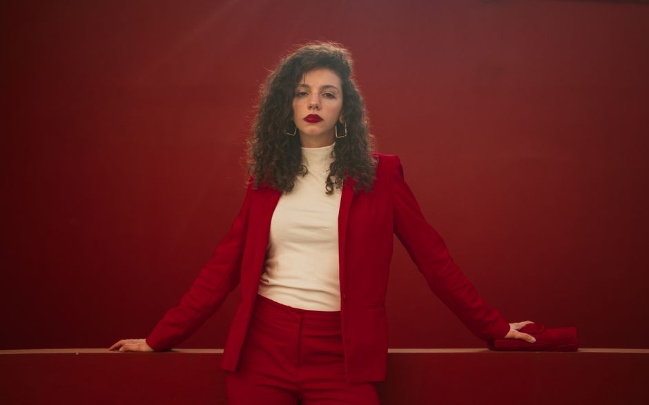 Elegant woman in a stylish red suit posing confidently in front of a matching red background.