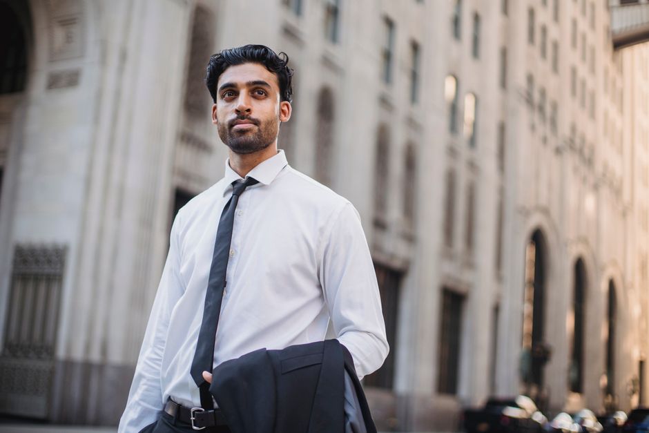 Young businessman with jacket over shoulder in cityscape background, looking confident.