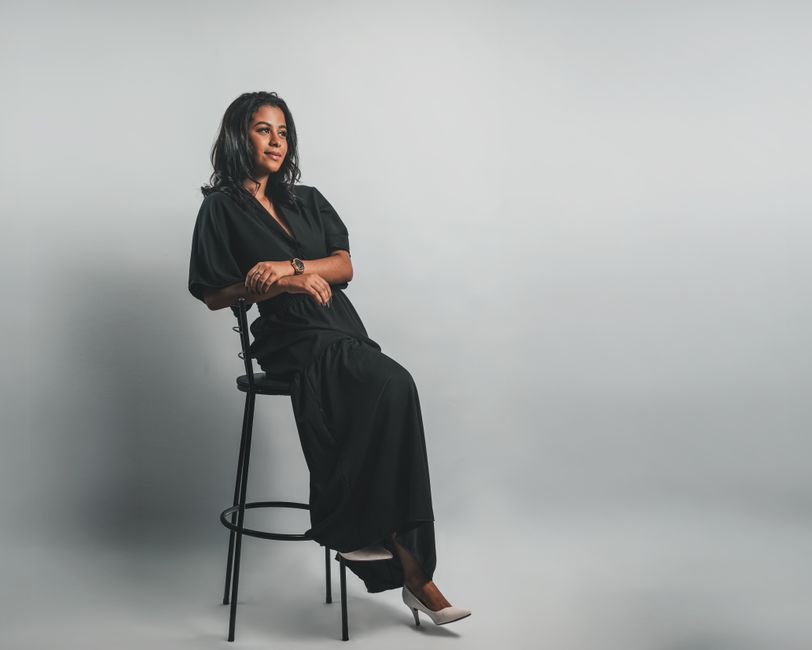 Elegant portrait of a woman seated on a stool in a minimalist studio setting.