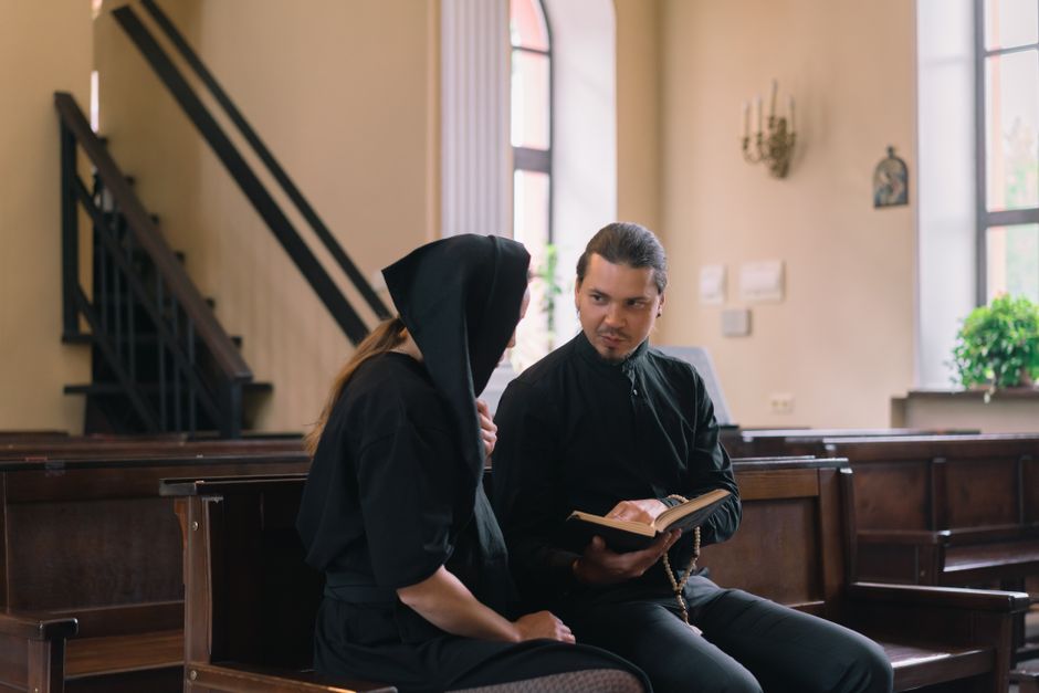 A priest and a woman in black clothing hold a religious discussion inside a church.