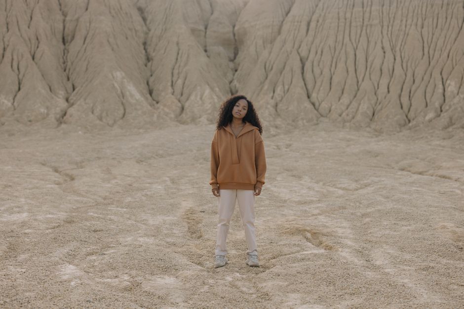 Model in a trendy outfit standing in a barren, desert-like landscape with a neutral tone.