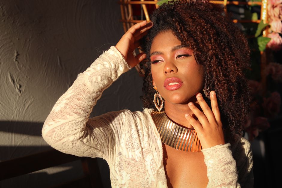 A stylish woman poses in sunlight with a textured wall backdrop, showcasing elegance.