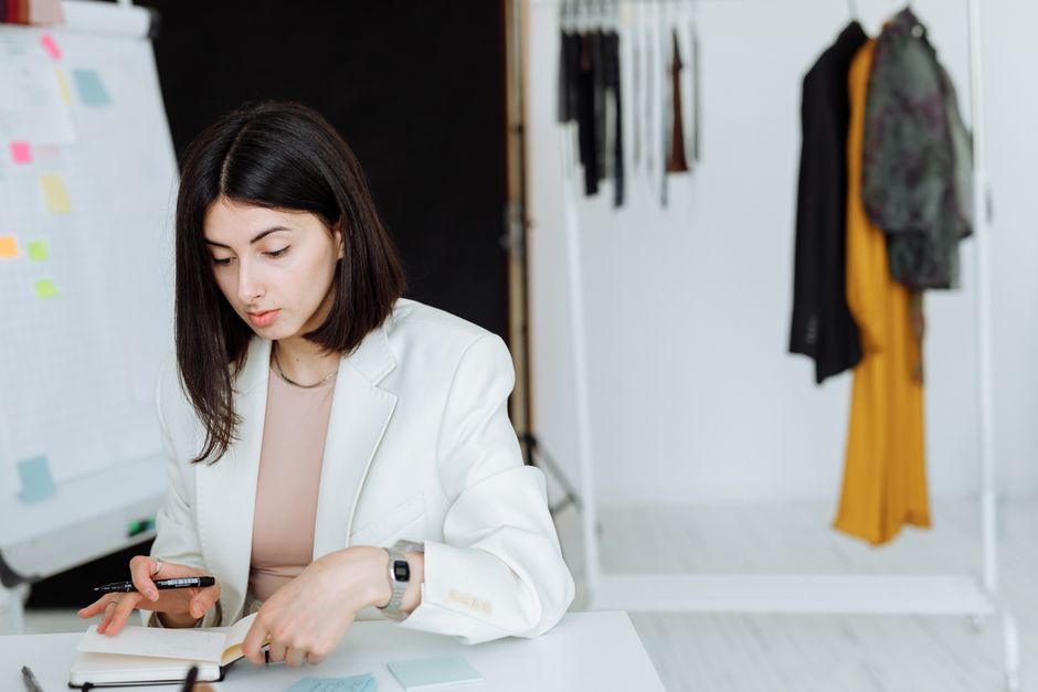 Young woman in white blazer writing notes in a modern fashion office. Stylish workspace.