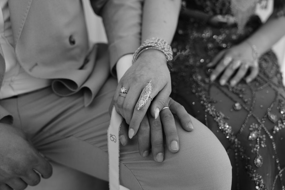 Close-up of a couple's hands adorned with intricate jewelry, in a monochrome setting.