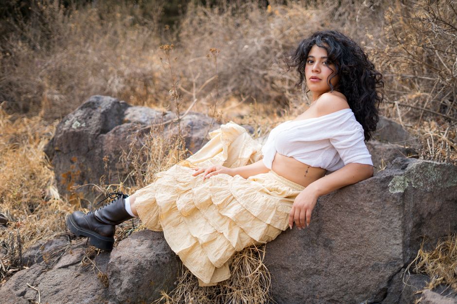 Woman in bohemian outfit reclining on rocks amidst dry grass, exuding a relaxed and natural vibe.