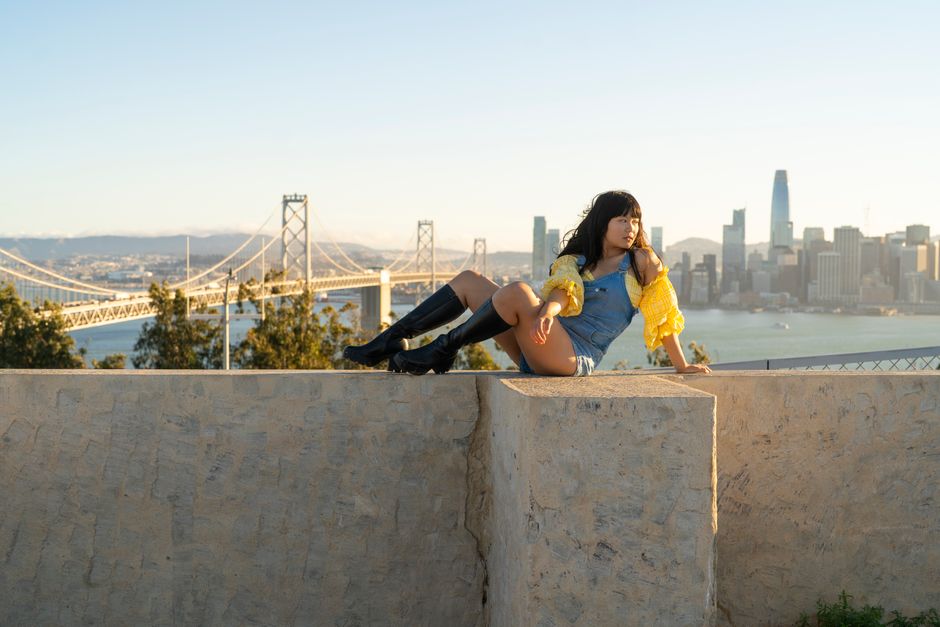 Young woman sitting on a ledge overlooking San Francisco and the Bay Bridge at sunset.