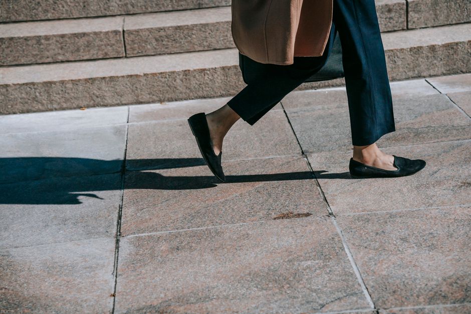 Crop anonymous female in trendy formal outfit strolling on paved sidewalk on sunny autumn day
