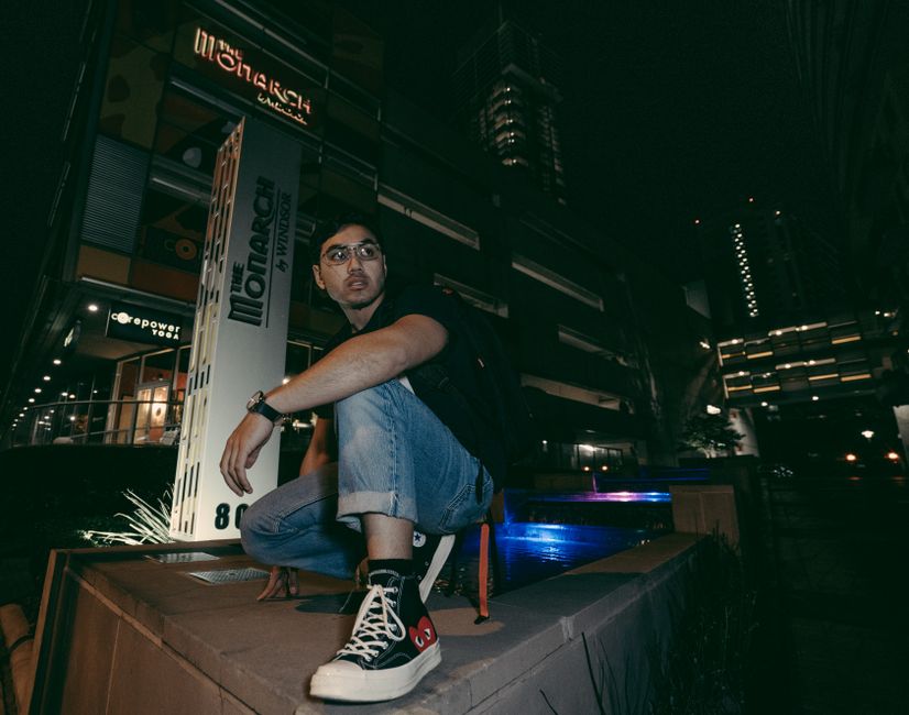 Man posing outdoors in urban setting illuminated by night city lights.