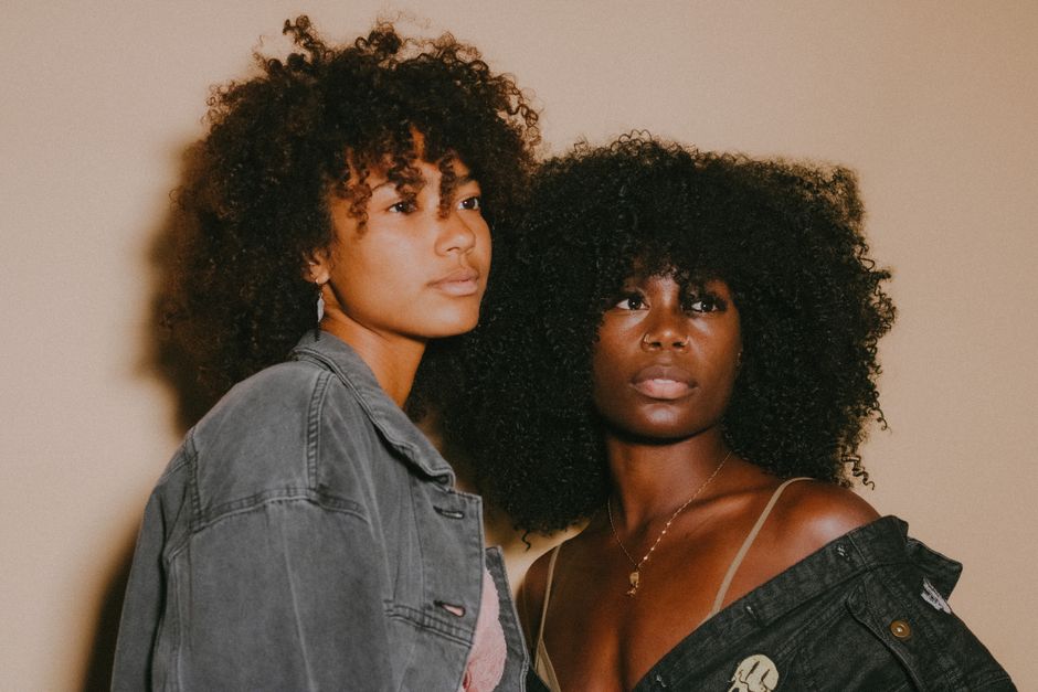 Captivating studio portrait featuring two young women with afro hair in denim jackets.