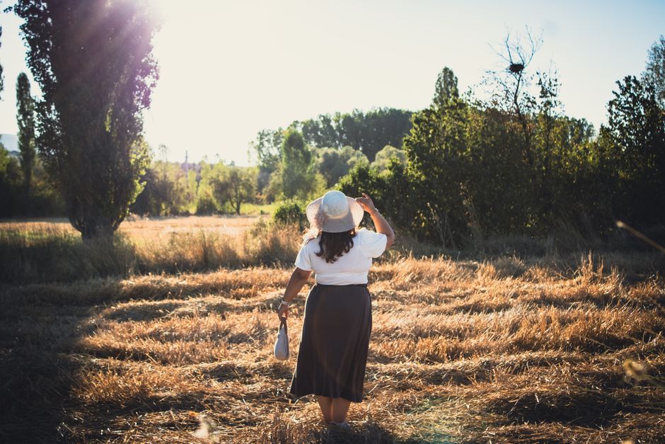 Woman in a sun hat walking through a sunny field, capturing a serene morning moment.