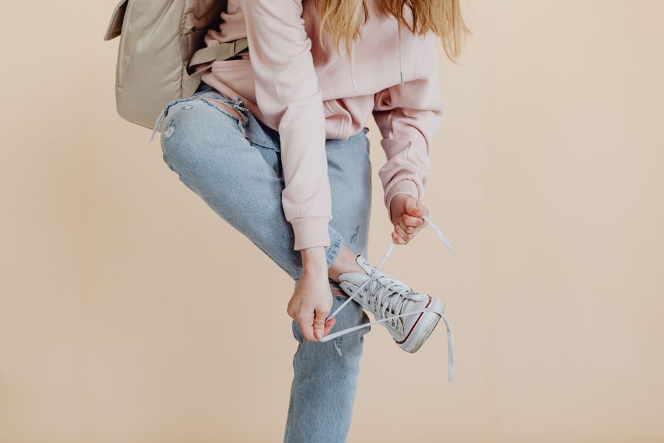 Casual fashion look with woman in denim and pink tying her white sneakers.