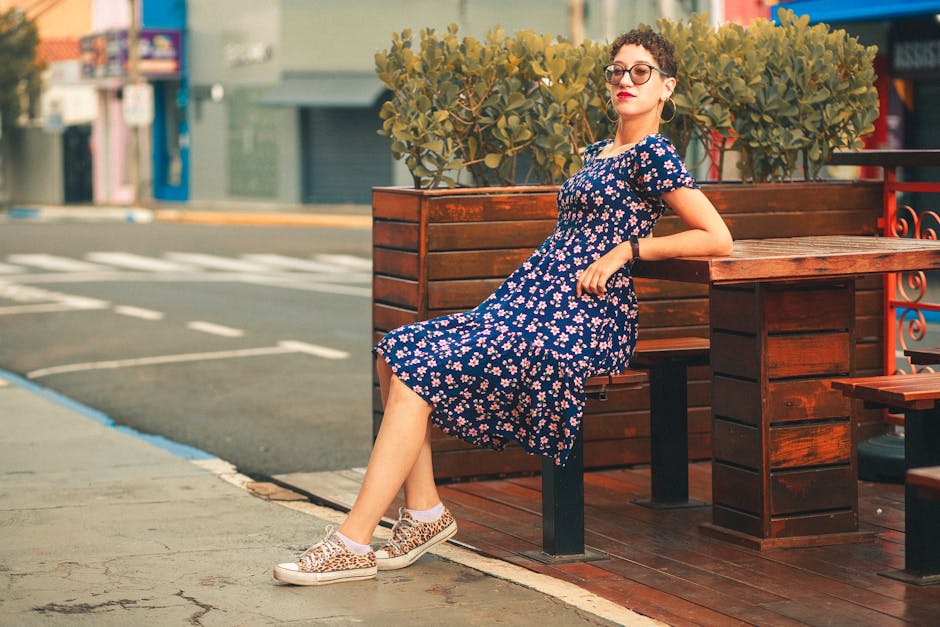 Stylish woman in a floral sundress relaxing outdoors by wooden table.