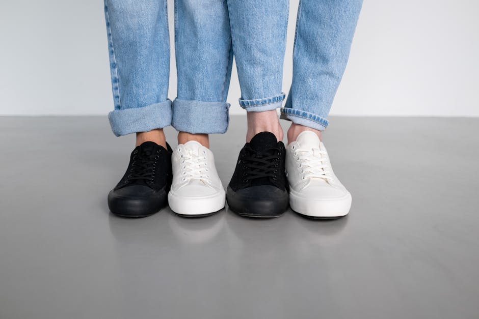 Close-up of three pairs of denim jeans and sneakers on a smooth floor.