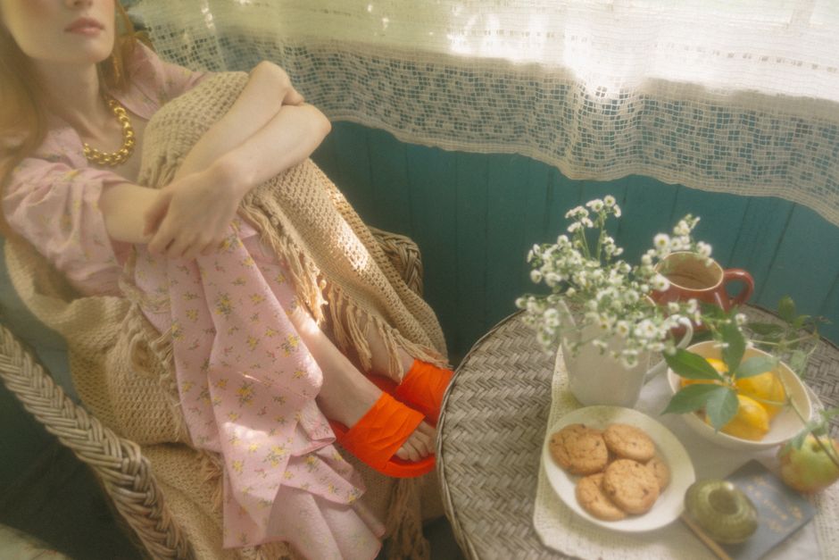 A woman in a floral dress enjoys a serene breakfast setting, with cookies and tea on a round table.